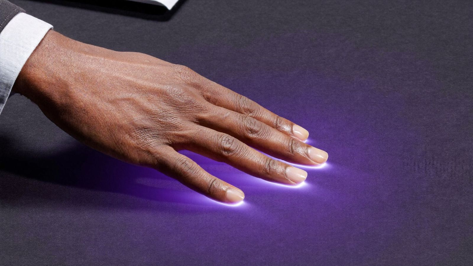 Una mano humana sobre una superficie que se ilumina con luz morada